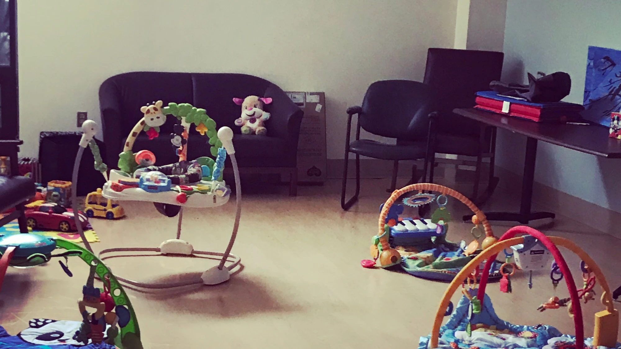 A room set up with a baby jumper, play gyms, and toys next to a couch